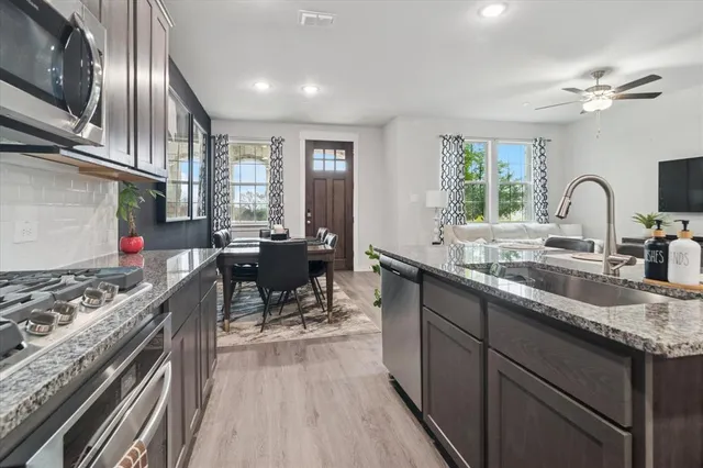 a kitchen with stainless steel appliances granite countertop a stove a sink dishwasher a dining table and chairs with wooden floor