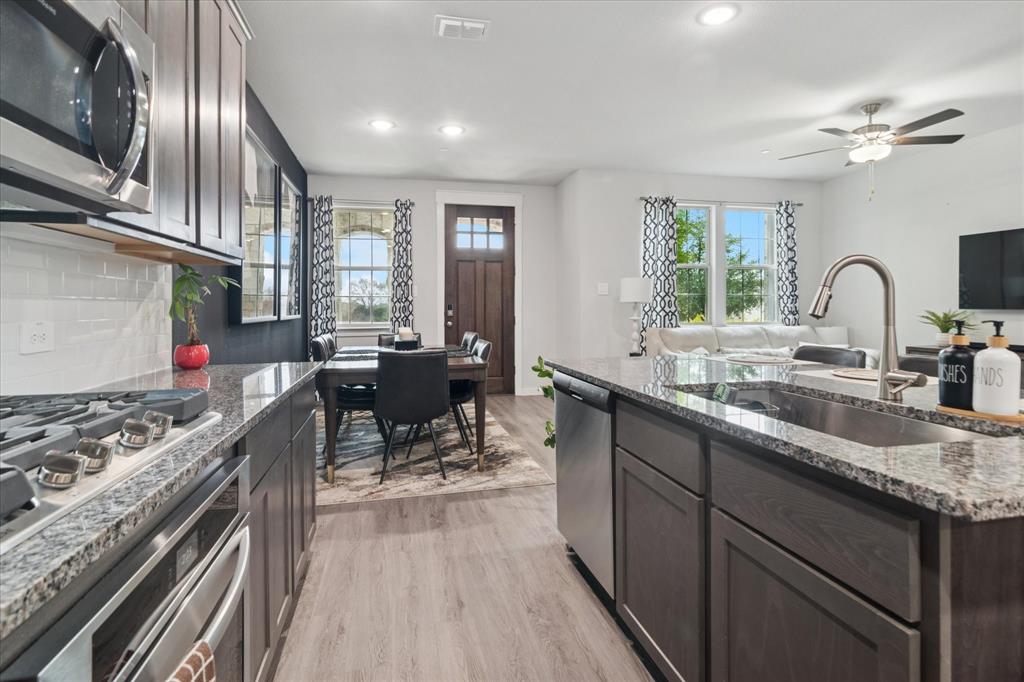 3047 Tenor Way Sachse, TX 75048 - Photo 5 of 17 a kitchen with stainless steel appliances granite countertop a stove a sink dishwasher a dining table and chairs with wooden floor