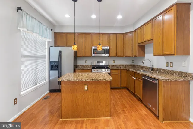 a kitchen with stainless steel appliances granite countertop a refrigerator a sink dishwasher a stove and a microwave oven with wooden floor