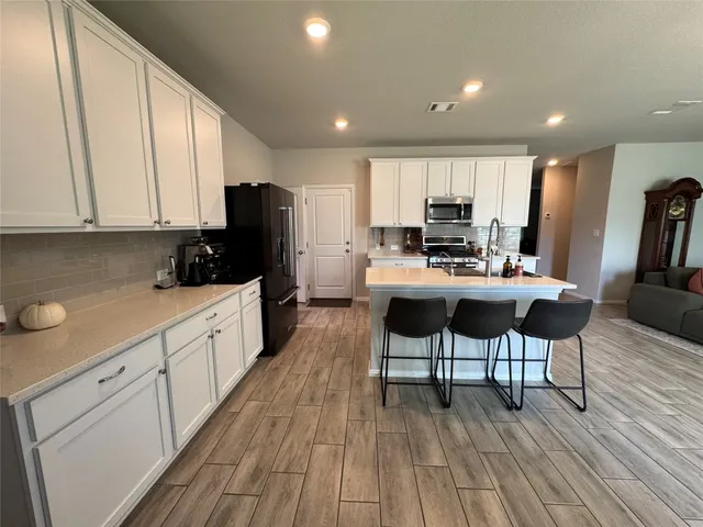 a kitchen with stainless steel appliances kitchen island granite countertop white cabinets a sink a stove a dining table and chairs with wooden floor