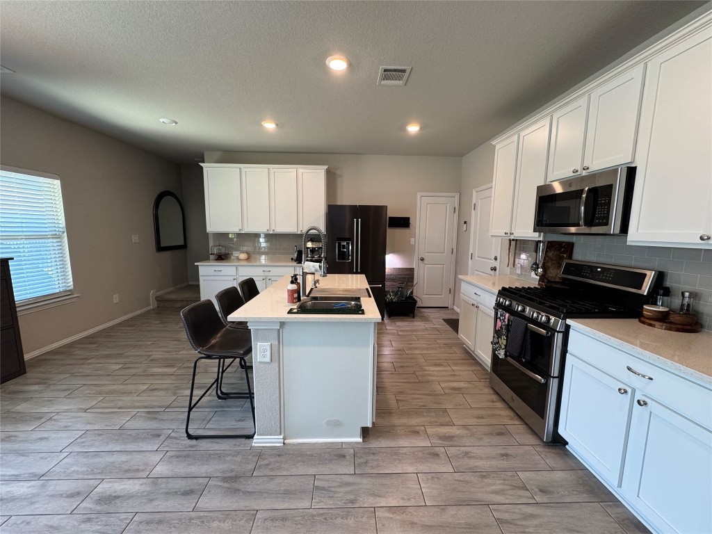 247 Simon Kyle, TX 78640 - Photo 4 of 23 a large white kitchen with stainless steel appliances granite countertop a stove a sink a microwave and a refrigerator