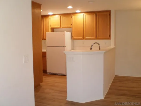a view of a refrigerator in kitchen and an empty room with wooden floor