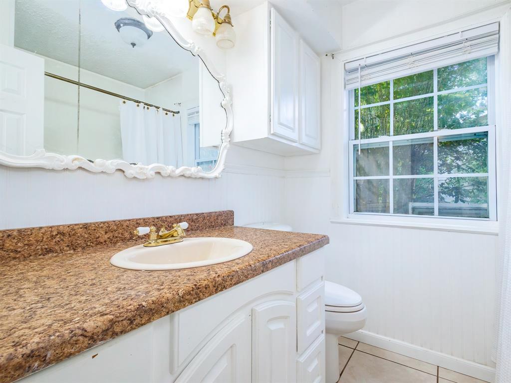 4002 Austin Avenue Brownwood, TX 76801 - Photo 25 of 34 a bathroom with a granite countertop sink a toilet a mirror and a window
