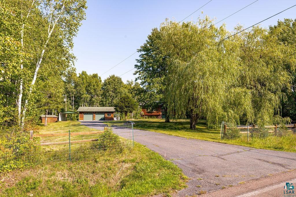 5370 Ugstad Road Hermantown, MN 55811 - Photo 54 of 68 Paved driveway leading to a detached two-car garage with overhead doors, surrounded by mature trees and natural landscaping