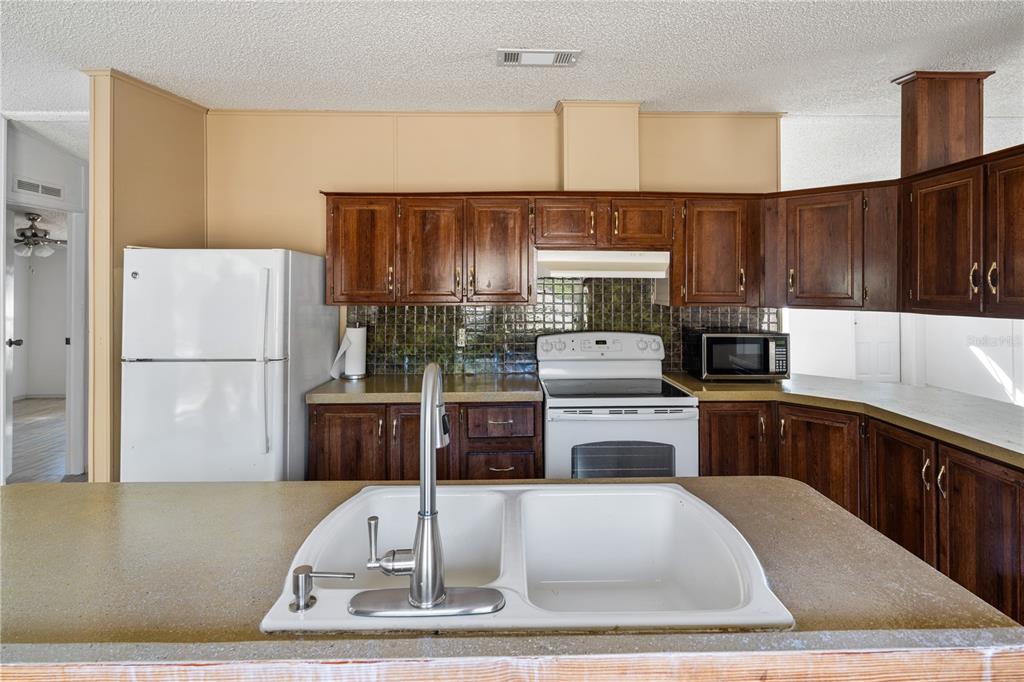 4495 Southeast 150th Street Summerfield, FL 34491 - Photo 61 of 76 a kitchen with a refrigerator a stove a sink dishwasher and wooden cabinets with wooden floor