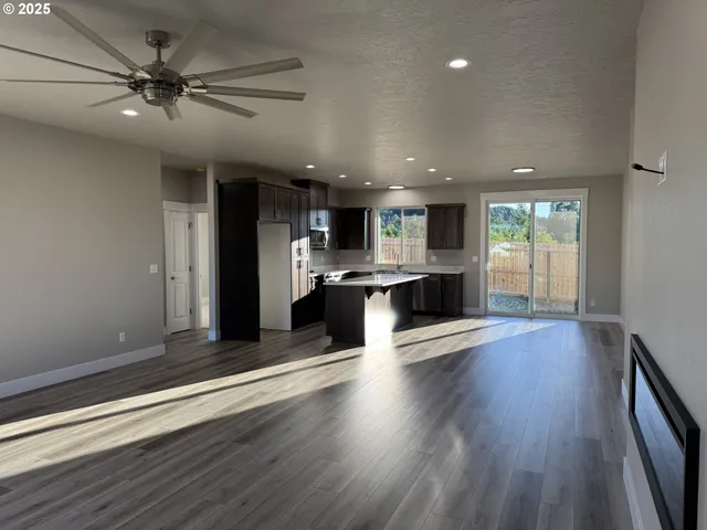 an empty room with wooden floor and kitchen view