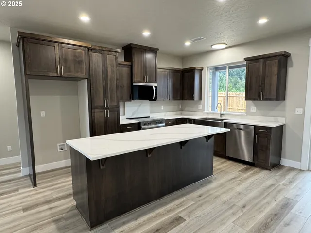 a large kitchen with stainless steel appliances kitchen island granite countertop a stove a refrigerator a sink and dishwasher with wooden floor