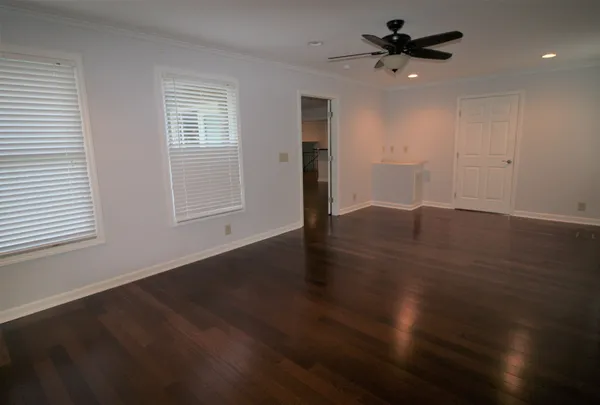 an empty room with wooden floor chandelier fan and windows