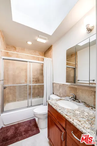 a bathroom with a granite countertop sink a toilet a mirror and bathtub