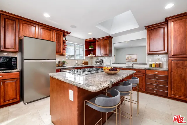 a kitchen with stainless steel appliances granite countertop a stove top oven a sink dishwasher and a refrigerator with wooden cabinets