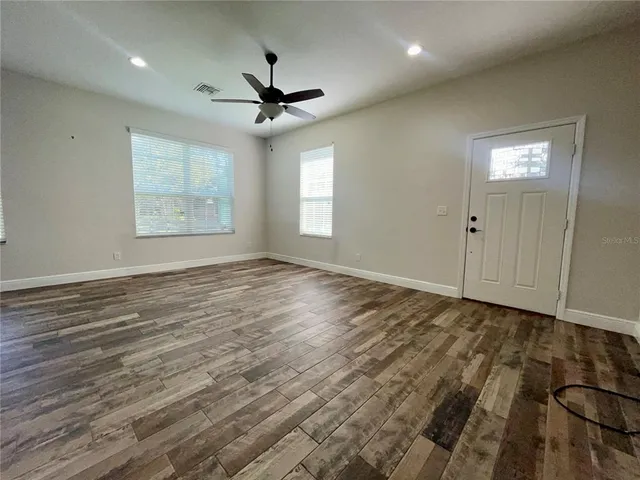 a view of an empty room and window a ceiling fan and wooden floor