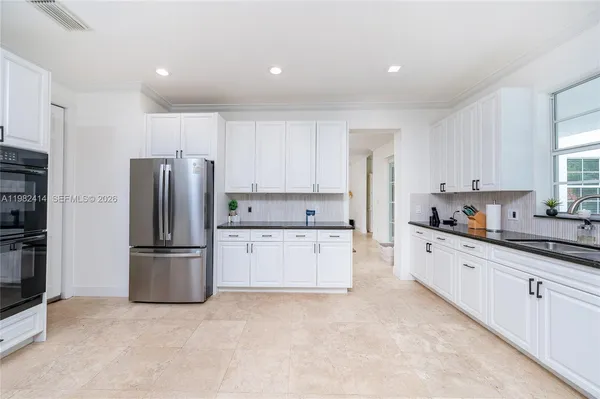 a kitchen with granite countertop white cabinets white appliances a large window and a sink