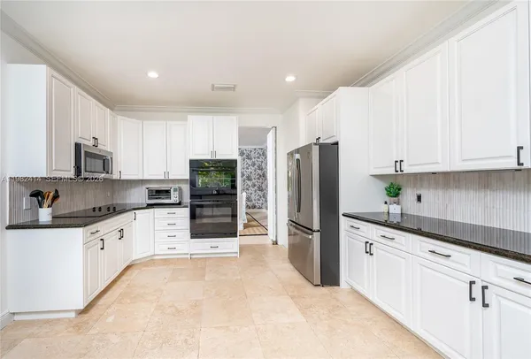 a kitchen with granite countertop a refrigerator sink and white cabinets