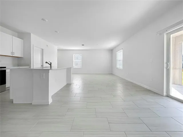 a view of an empty room with kitchen and window
