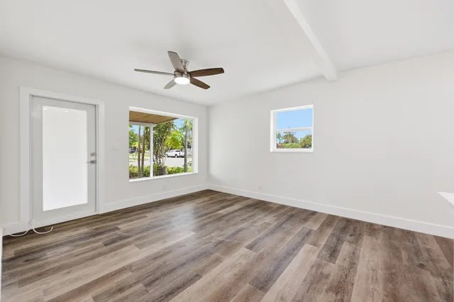 an empty room with wooden floor chandelier fan and windows