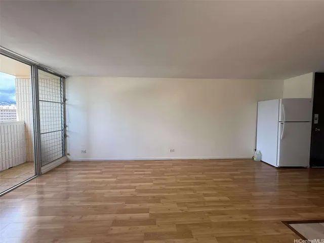 a view of an empty room with wooden floor and a refrigerator