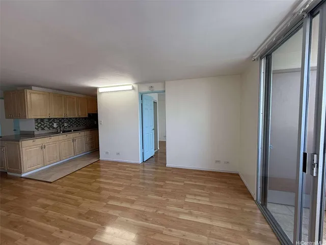 a view of an empty room with kitchen and window