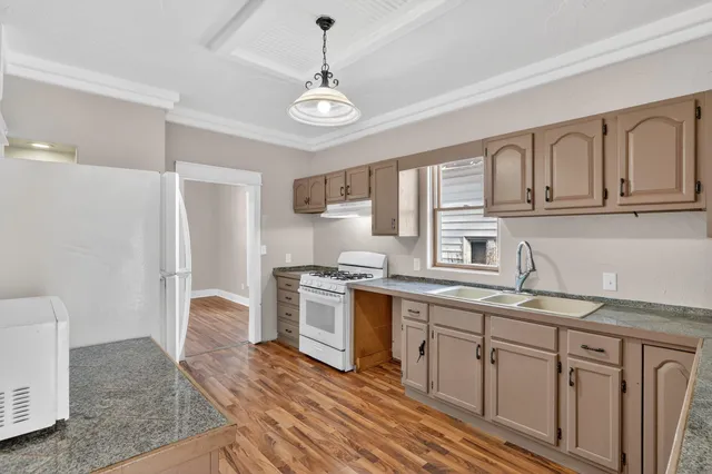 a kitchen with stainless steel appliances granite countertop a refrigerator a sink dishwasher a stove and white countertops with wooden floor