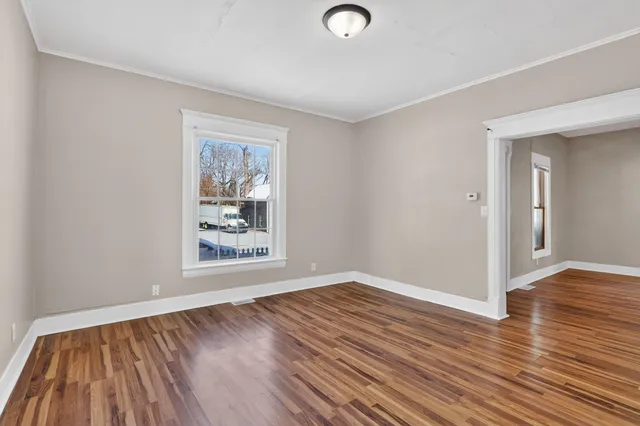 a view of an empty room with wooden floor and a window