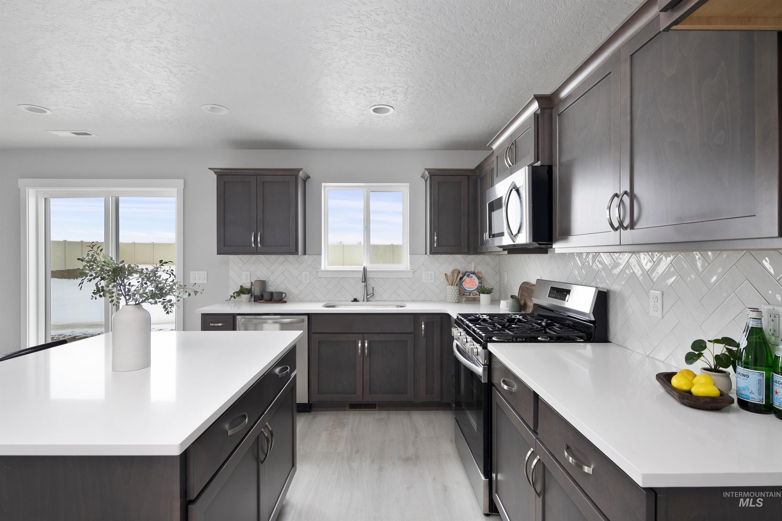 444 South Bobby Way Kuna, ID 83634 - Photo 4 of 6 Kitchen featuring appliances with stainless steel finishes, decorative backsplash, a center island, a textured ceiling, and light wood-style floors