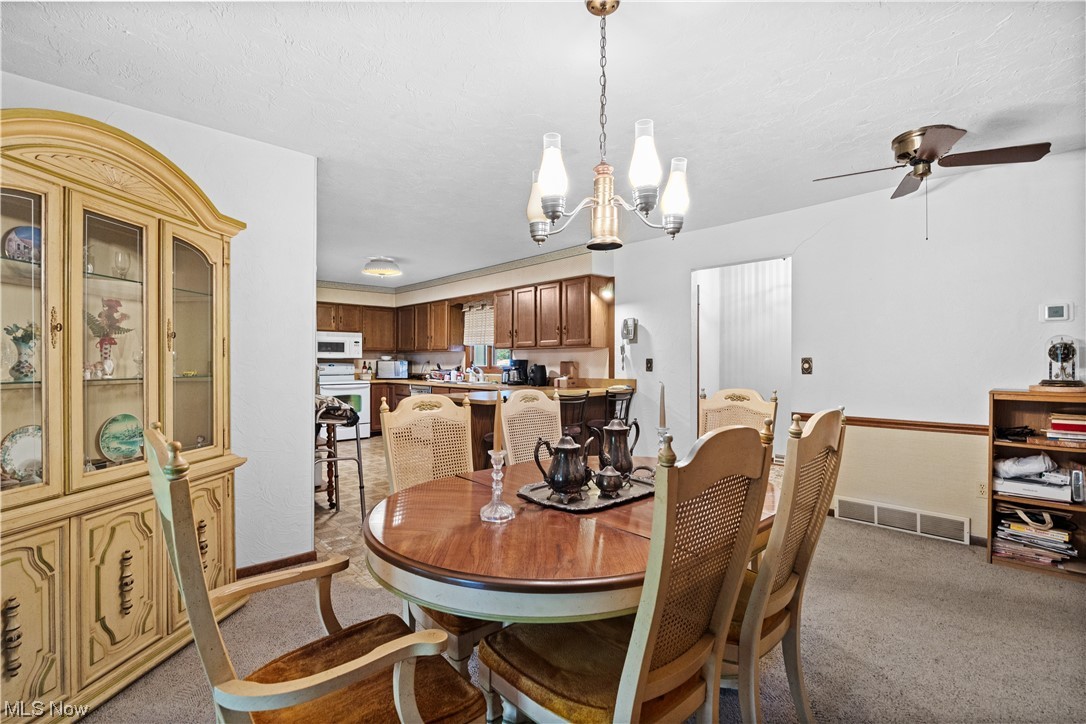 Carpeted dining area featuring ceiling fan with notable chandelier