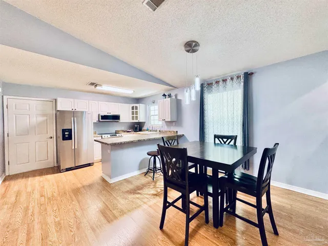 a kitchen with stainless steel appliances kitchen island granite countertop a dining table chairs and a refrigerator