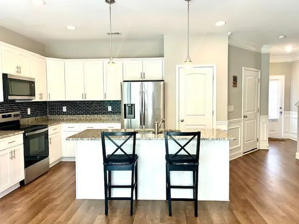 a kitchen with stainless steel appliances granite countertop a stove a sink a microwave a refrigerator and white cabinets with wooden floor