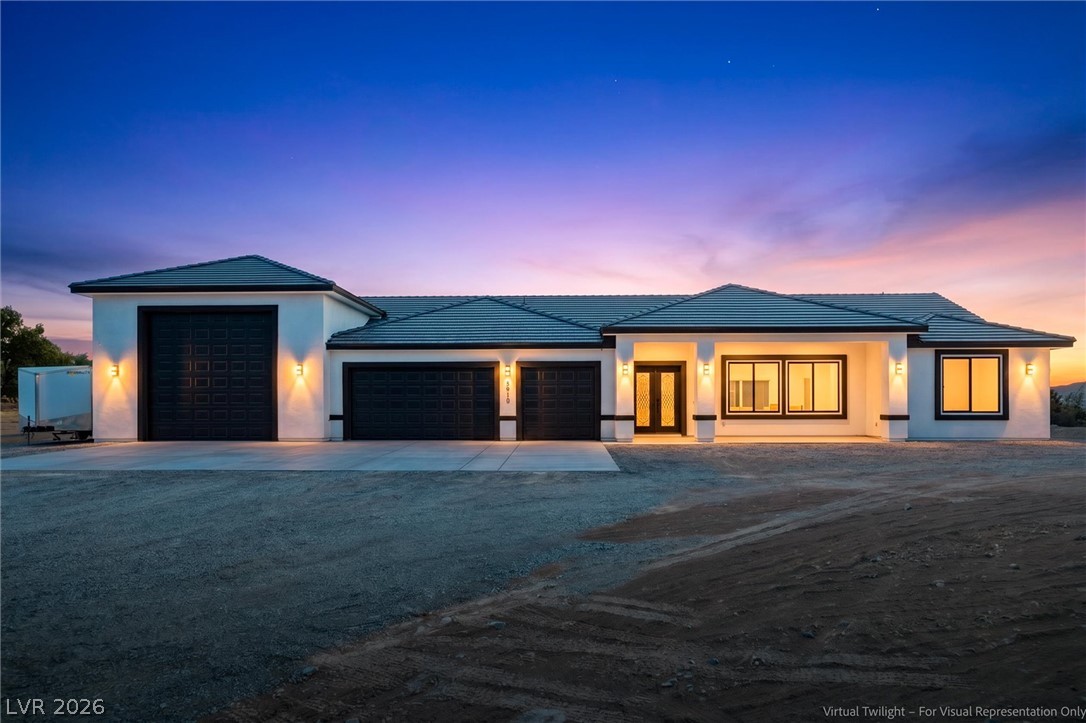 5910 East Kellogg Road Pahrump, NV 89061 - Photo 4 of 58 A striking modern ranch, featuring a prominent three-car garage and luminous entry under a vibrant twilight sky.