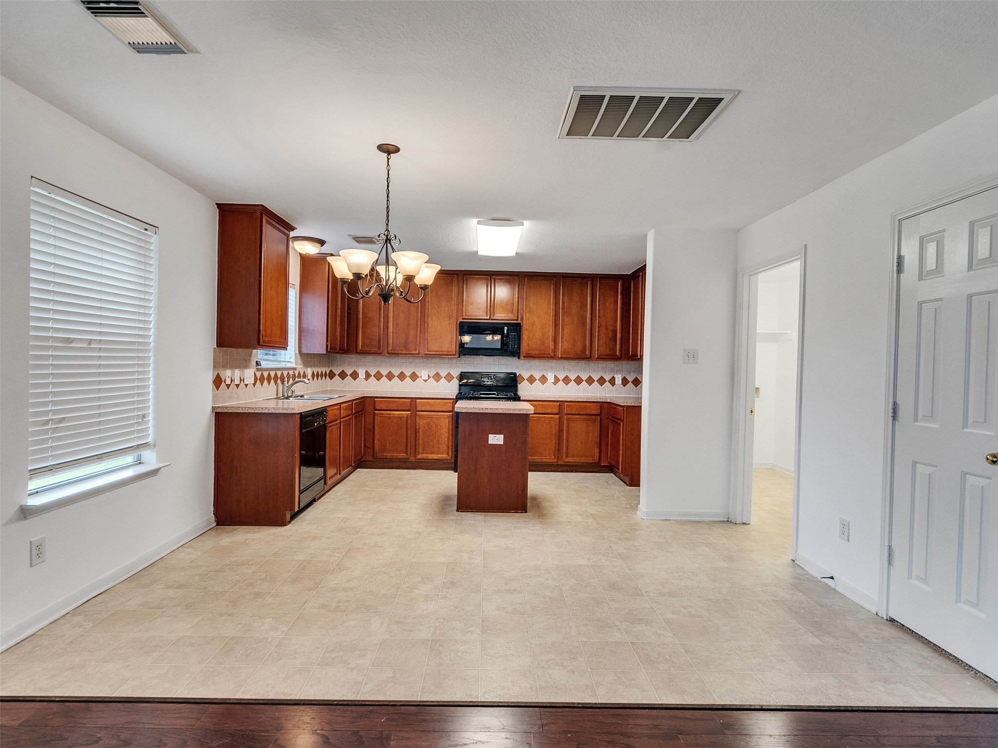 3307 Manor Tree Lane Houston, TX 77068 - Photo 11 of 44 This photo showcases a spacious kitchen with warm wooden cabinets, a central island, and a tile backsplash. The area features modern appliances, ample counter space, and a cozy dining nook under a stylish chandelier. Natural light streams through a window, enhancing the inviting atmosphere.