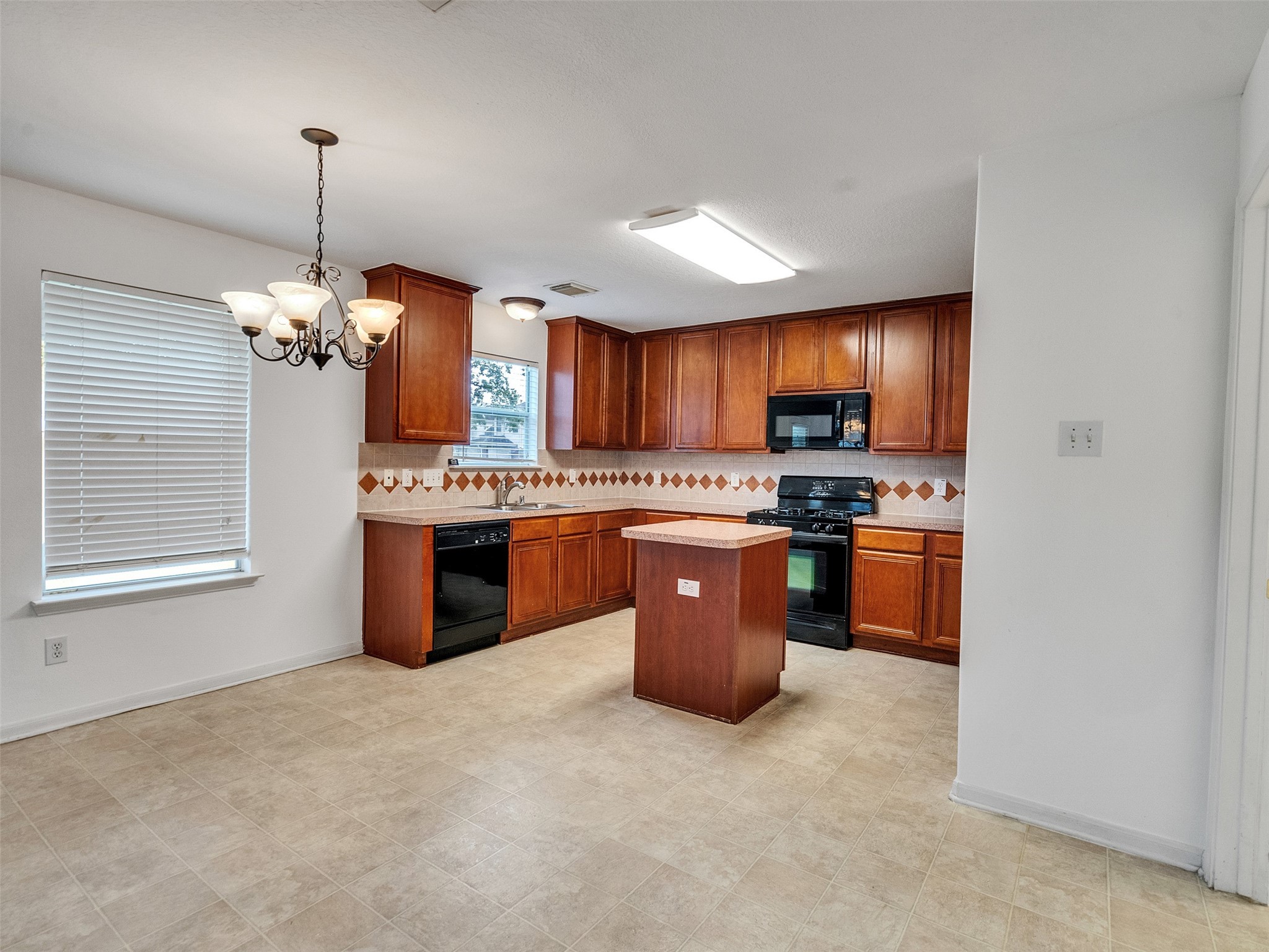 3307 Manor Tree Lane Houston, TX 77068 - Photo 12 of 44 This spacious kitchen features rich wood cabinetry, a central island, and modern black appliances. The dining area is highlighted by a stylish chandelier, and the room has ample natural light from a large window with blinds. The tile flooring adds a practical and elegant touch.