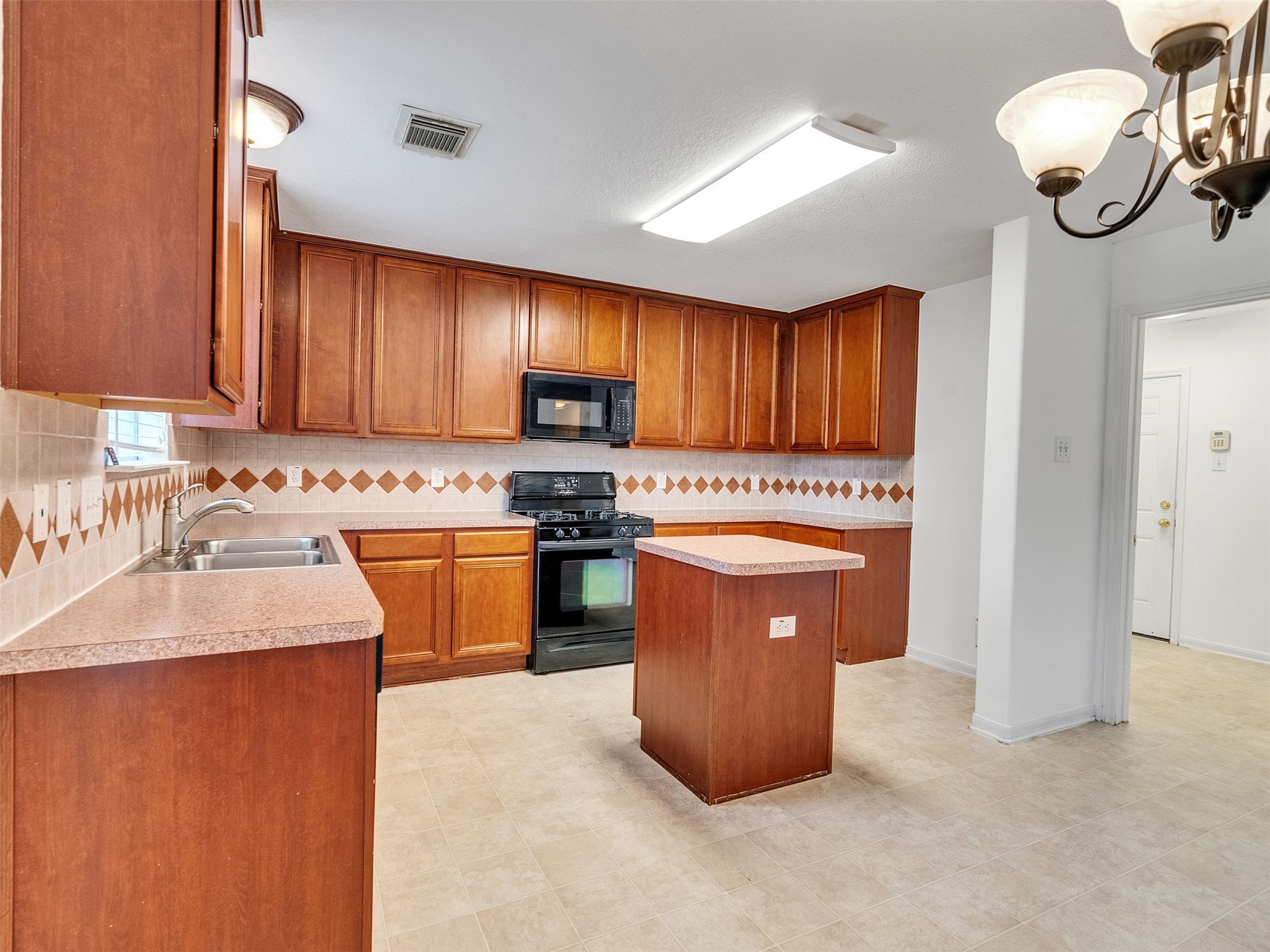 3307 Manor Tree Lane Houston, TX 77068 - Photo 16 of 44 This spacious kitchen features ample wooden cabinetry, a central island, and modern appliances. The neutral tile backsplash with diamond accents complements the countertops, while a hanging light fixture adds elegance to the dining area.