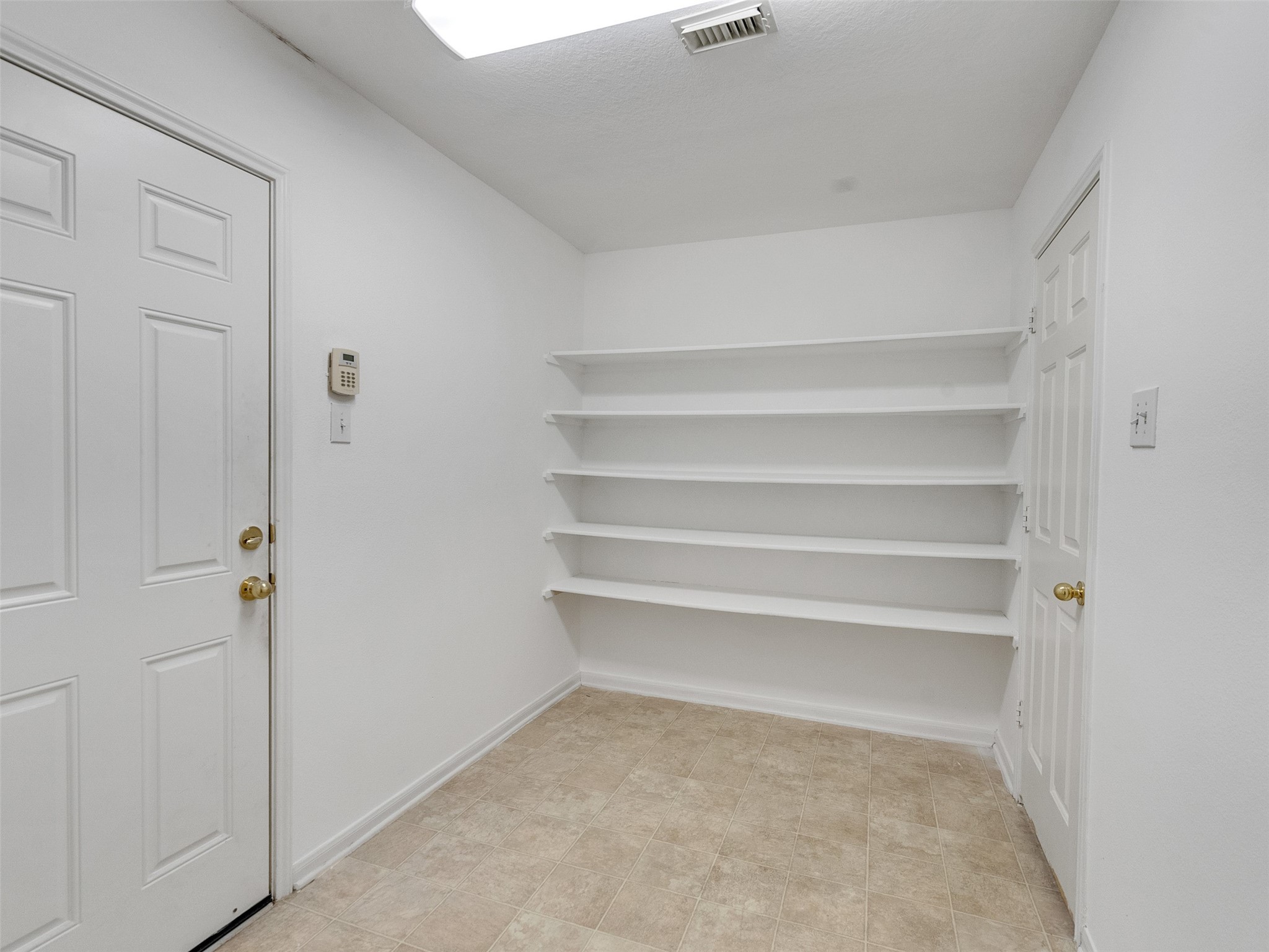 3307 Manor Tree Lane Houston, TX 77068 - Photo 18 of 44 This photo shows a small utility room with white walls, featuring built-in shelves and a tiled floor. There are two doors, one with a keypad lock, making it ideal for storage or as a pantry space.