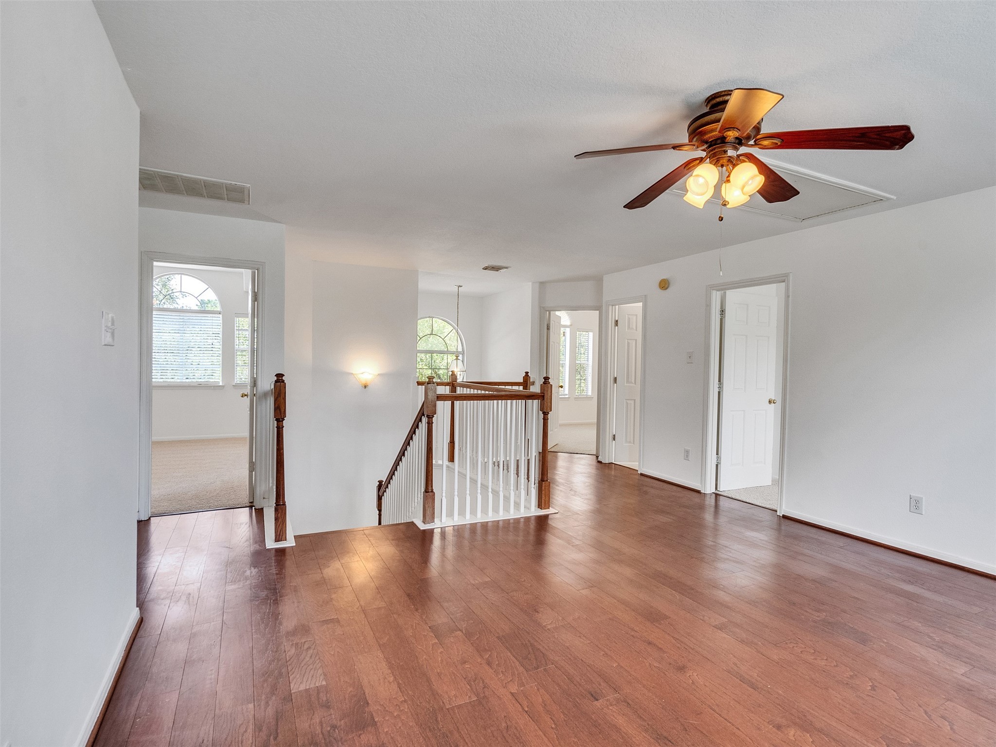 3307 Manor Tree Lane Houston, TX 77068 - Photo 20 of 44 Bright and spacious game room upper-level area with hardwood floors and a ceiling fan, featuring multiple doorways leading to bedrooms and bathrooms, and a central staircase with wooden railing.