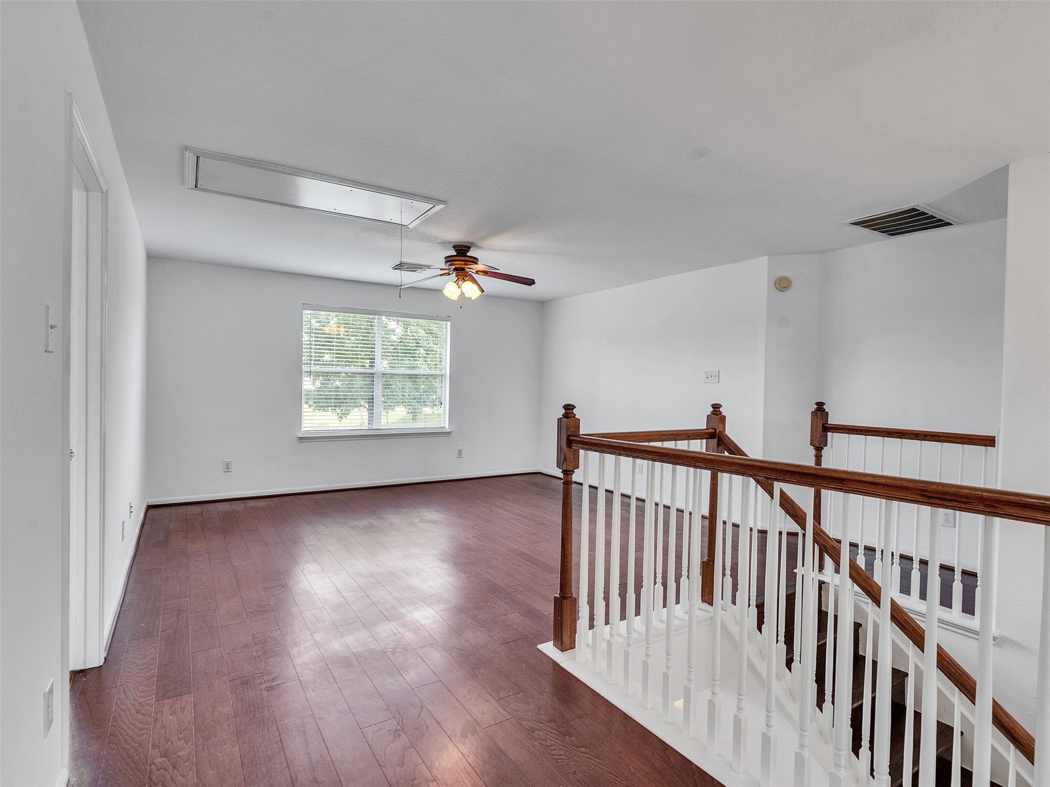 3307 Manor Tree Lane Houston, TX 77068 - Photo 25 of 44 Bright, spacious game room with hardwood floors, white walls, and a ceiling fan. Features a large window for natural light and a wooden railing overlooking a staircase. Ideal for a living or family area.