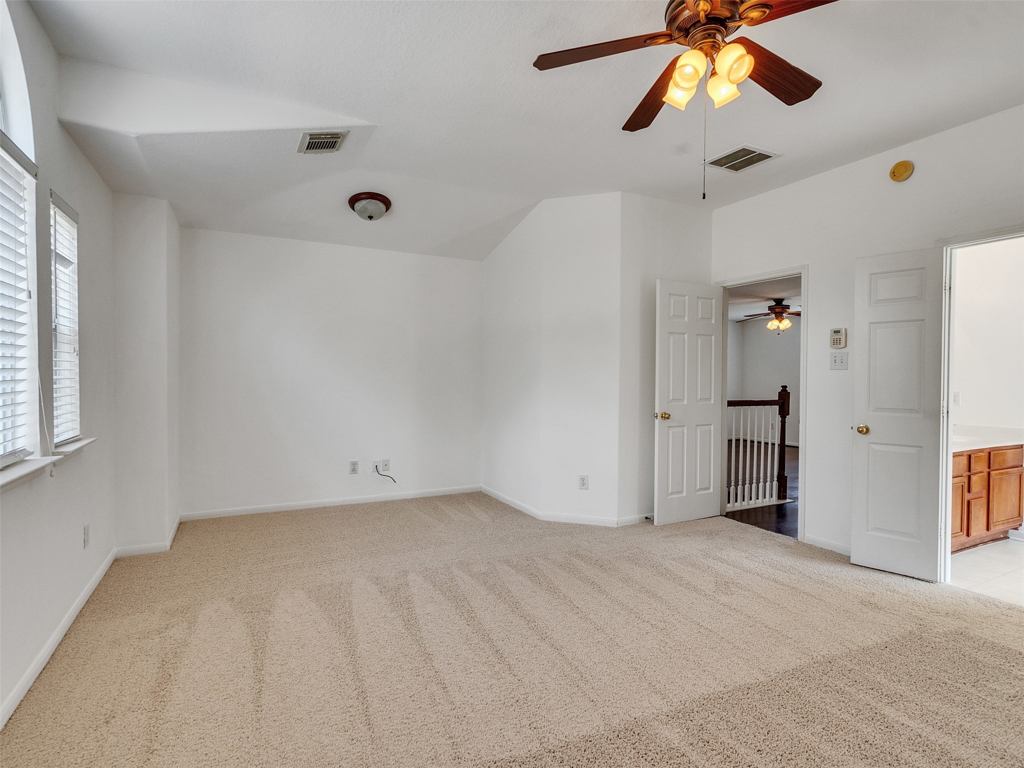 3307 Manor Tree Lane Houston, TX 77068 - Photo 27 of 44 Another angle of this spacious, carpeted master room features neutral tones, a ceiling fan, and ample natural light from large windows. It's well-connected to an adjacent hallway and bathroom, making it versatile for various uses.