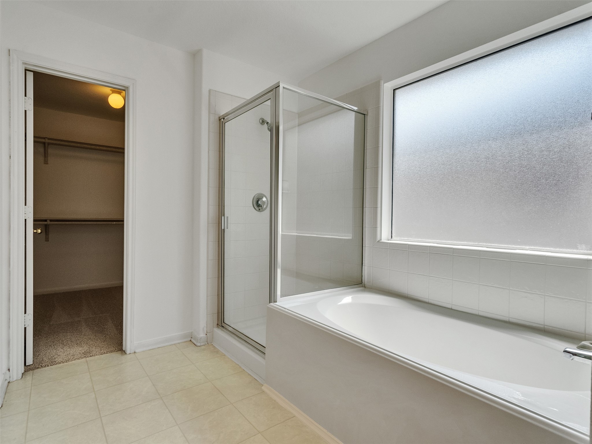 3307 Manor Tree Lane Houston, TX 77068 - Photo 29 of 44 Master bathroom features a spacious layout with a glass-enclosed shower, a large bathtub, and a frosted window for privacy. There's also an adjoining walk-in closet with ample storage space.