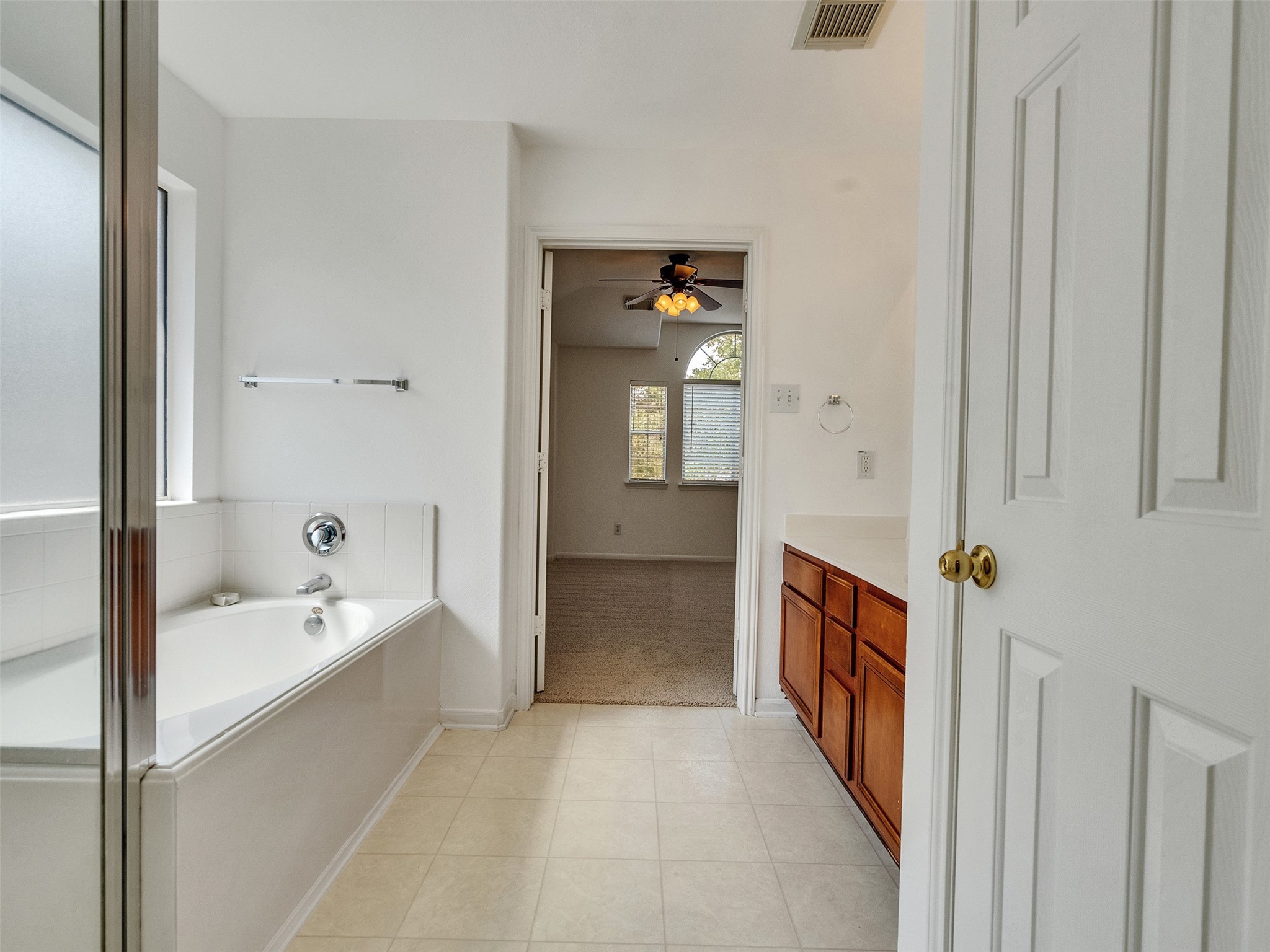 3307 Manor Tree Lane Houston, TX 77068 - Photo 31 of 44 Bright master bathroom with a large soaking tub, adjacent shower, and a vanity with wooden cabinets. The room connects to a carpeted area with a ceiling fan and an arched window.