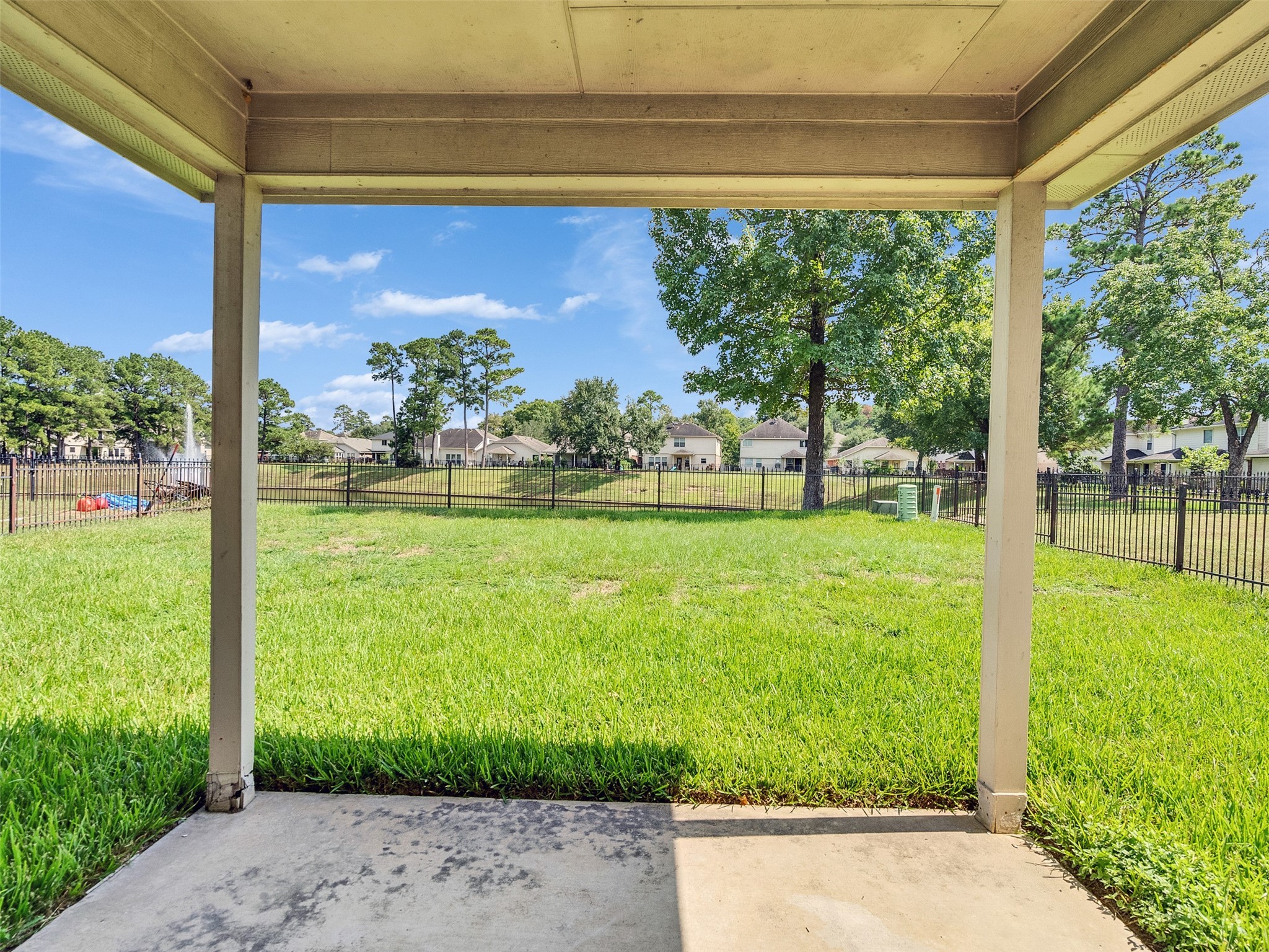 3307 Manor Tree Lane Houston, TX 77068 - Photo 38 of 44 This photo showcases a covered patio overlooking a spacious, fenced backyard with a view of neighboring houses and mature trees under a clear blue sky. Ideal for outdoor relaxation and activities.