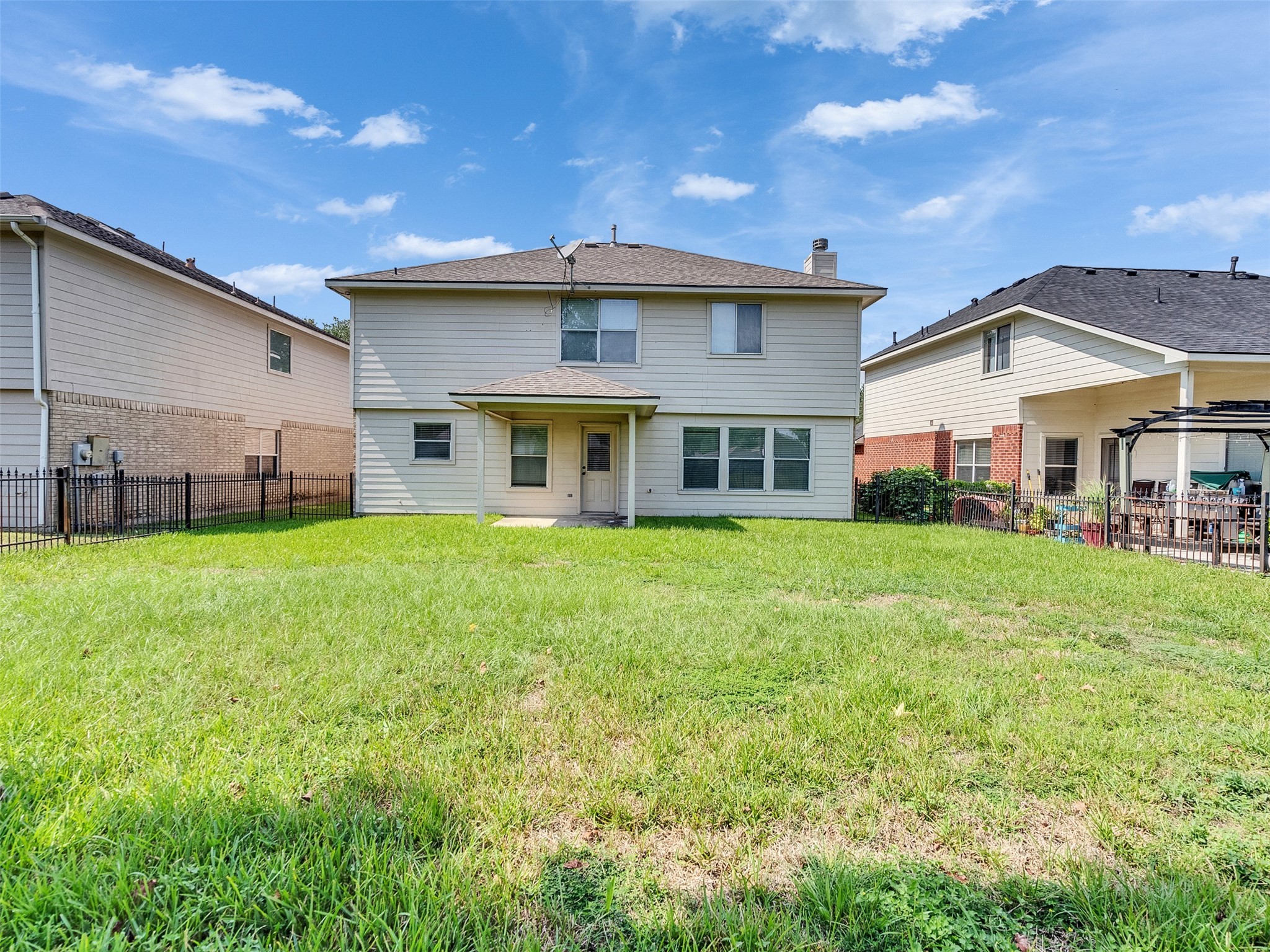 3307 Manor Tree Lane Houston, TX 77068 - Photo 40 of 44 This photo shows the backyard of a two-story house with a large, open lawn. The exterior is light-colored with multiple windows, and there's a small covered patio area. It’s flanked by neighboring houses and has a fenced perimeter.