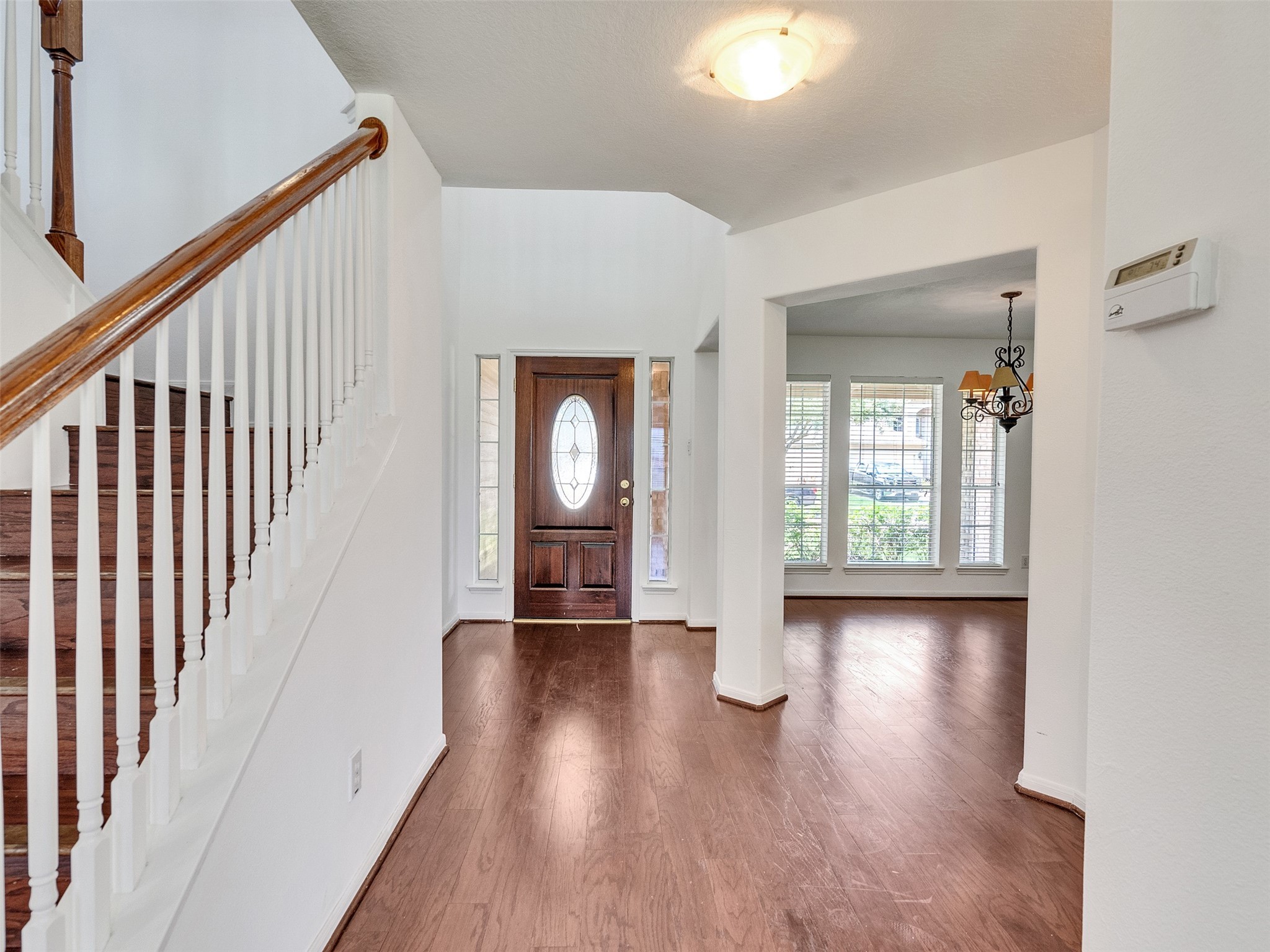 3307 Manor Tree Lane Houston, TX 77068 - Photo 6 of 44 Bright entryway with hardwood floors, featuring a staircase with wooden railing. The area leads to a room with large windows and a decorative chandelier, creating an inviting and open atmosphere.