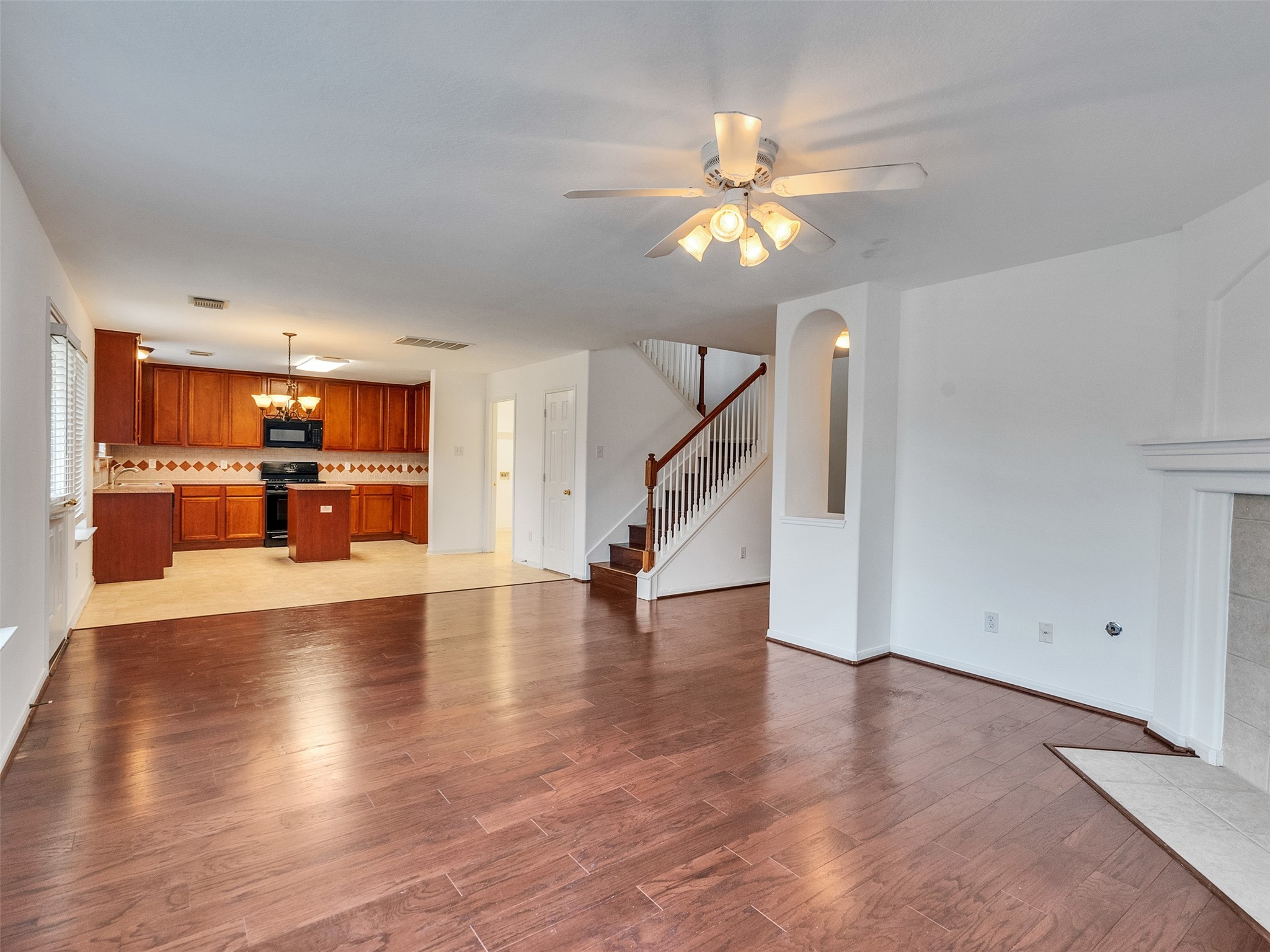 3307 Manor Tree Lane Houston, TX 77068 - Photo 8 of 44 This spacious open-concept living area features hardwood floors, a cozy fireplace, and a ceiling fan. The kitchen boasts warm wood cabinetry, a tiled backsplash, and modern appliances. A staircase leads to the upper level, and large windows provide ample natural light.