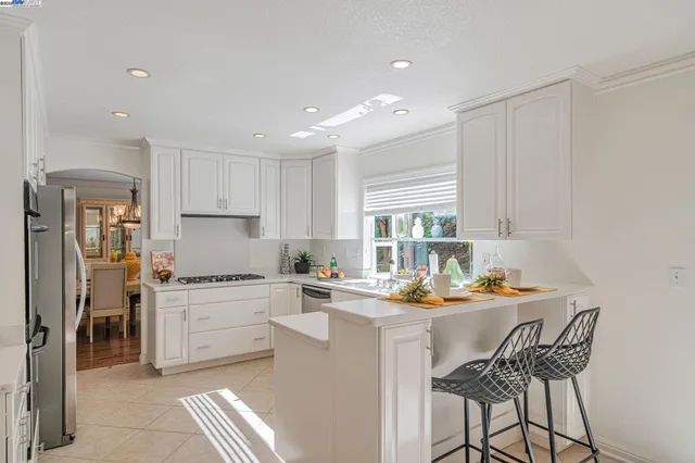 a room with stainless steel appliances kitchen island granite countertop a stove a sink a refrigerator and white cabinets with wooden floor