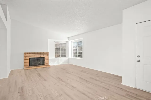 a view of an empty room with wooden floor fireplace and a window