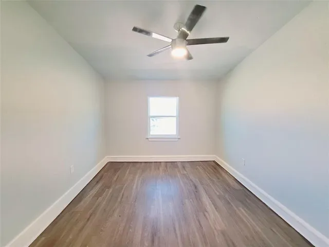 an empty room with wooden floor ceiling fan and windows