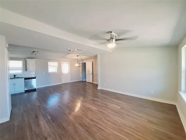 a view of an empty room with wooden floor and a ceiling fan