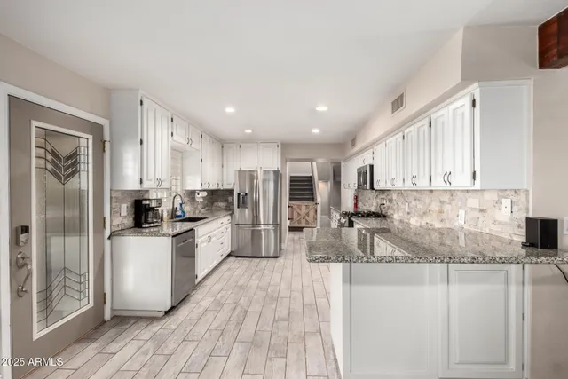 a kitchen with stainless steel appliances granite countertop a refrigerator a stove top oven a sink and dishwasher with wooden floor