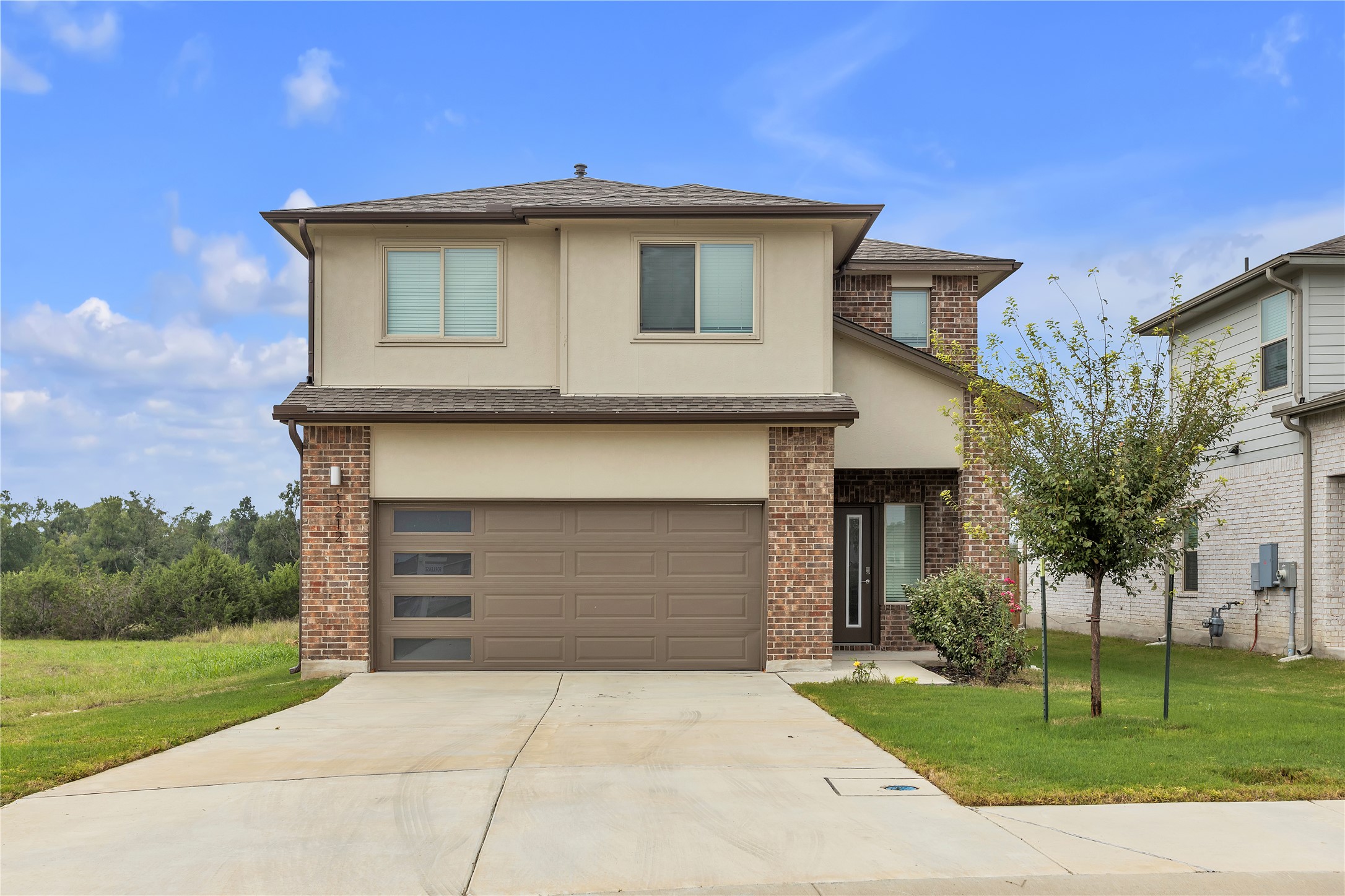 A modern facade with a striking brick and stucco exterior, boasting a contemporary garage door and well-kept front landscaping.