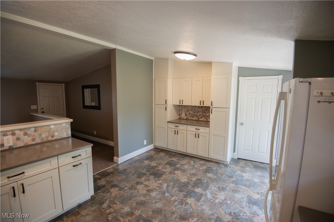 4594 Center Road Andover, OH 44003 - Photo 6 of 39 Kitchen featuring backsplash, freestanding refrigerator, lofted ceiling, a textured ceiling, and white cabinetry