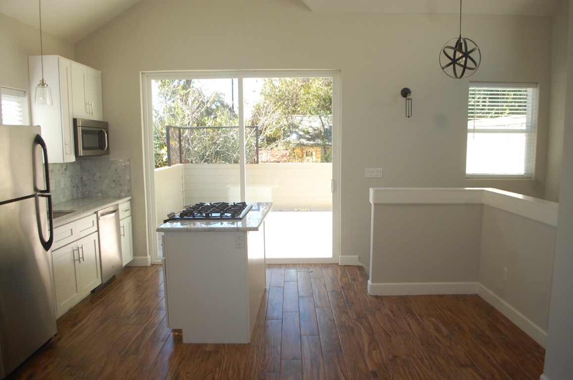 1707 Garden Street, Unit B Austin, TX 78702 - Photo 18 of 33 Kitchen featuring hanging light fixtures, white cabinets, appliances with stainless steel finishes, dark wood-style flooring, and light stone countertops