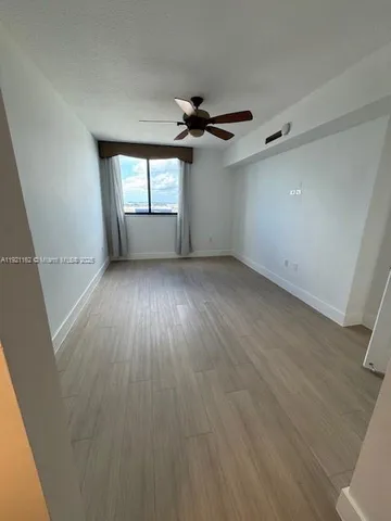 an empty room with wooden floor ceiling fan and windows